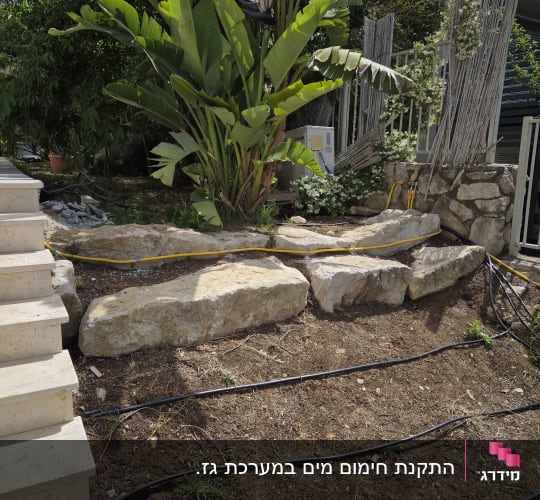 צינורות השקיה בגינה עם צמחייה וסלעים
